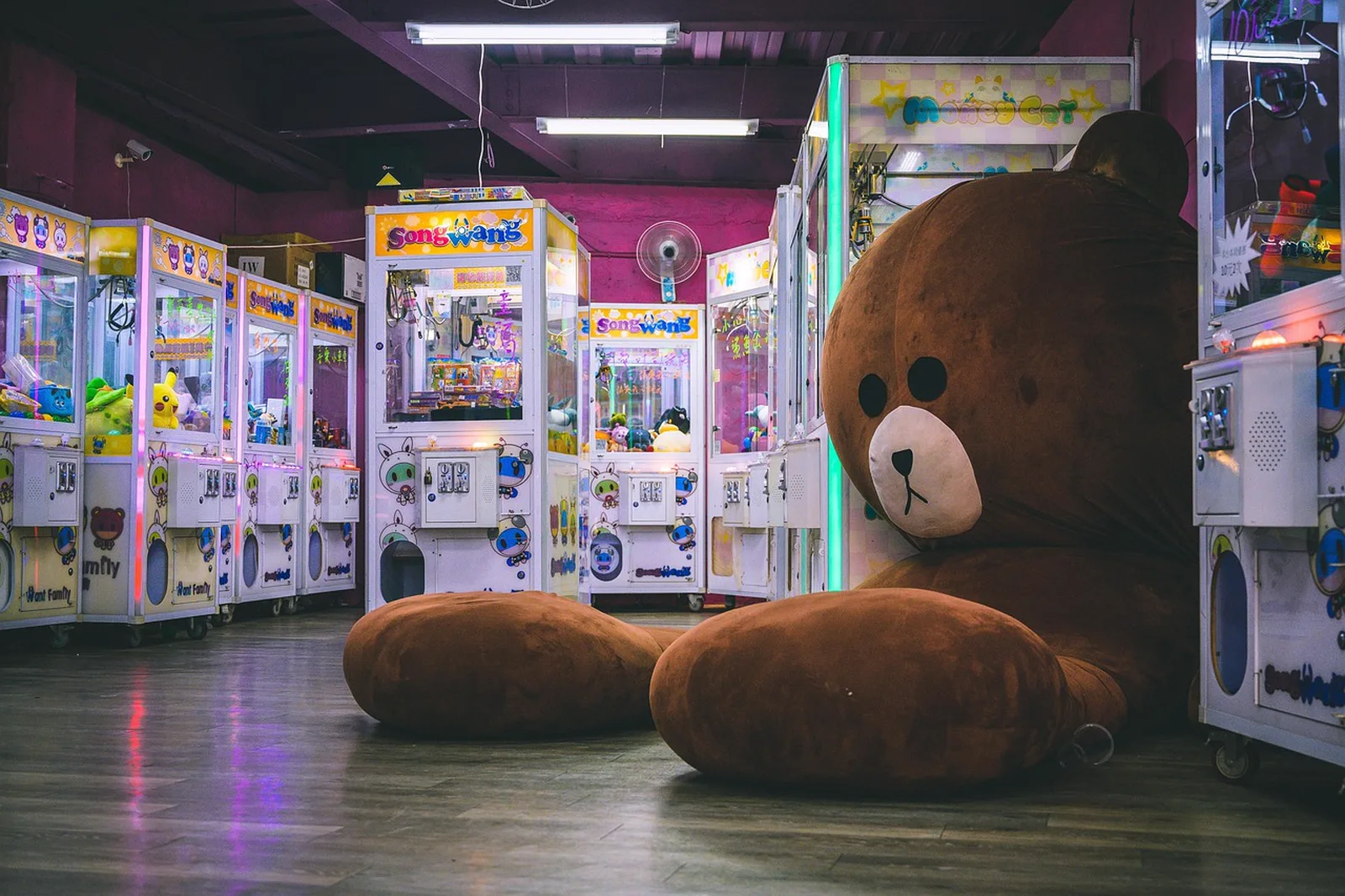 Fun Fair: Rows of arcade claw machines line a room with a giant brown plush teddy bear resting on the floor.