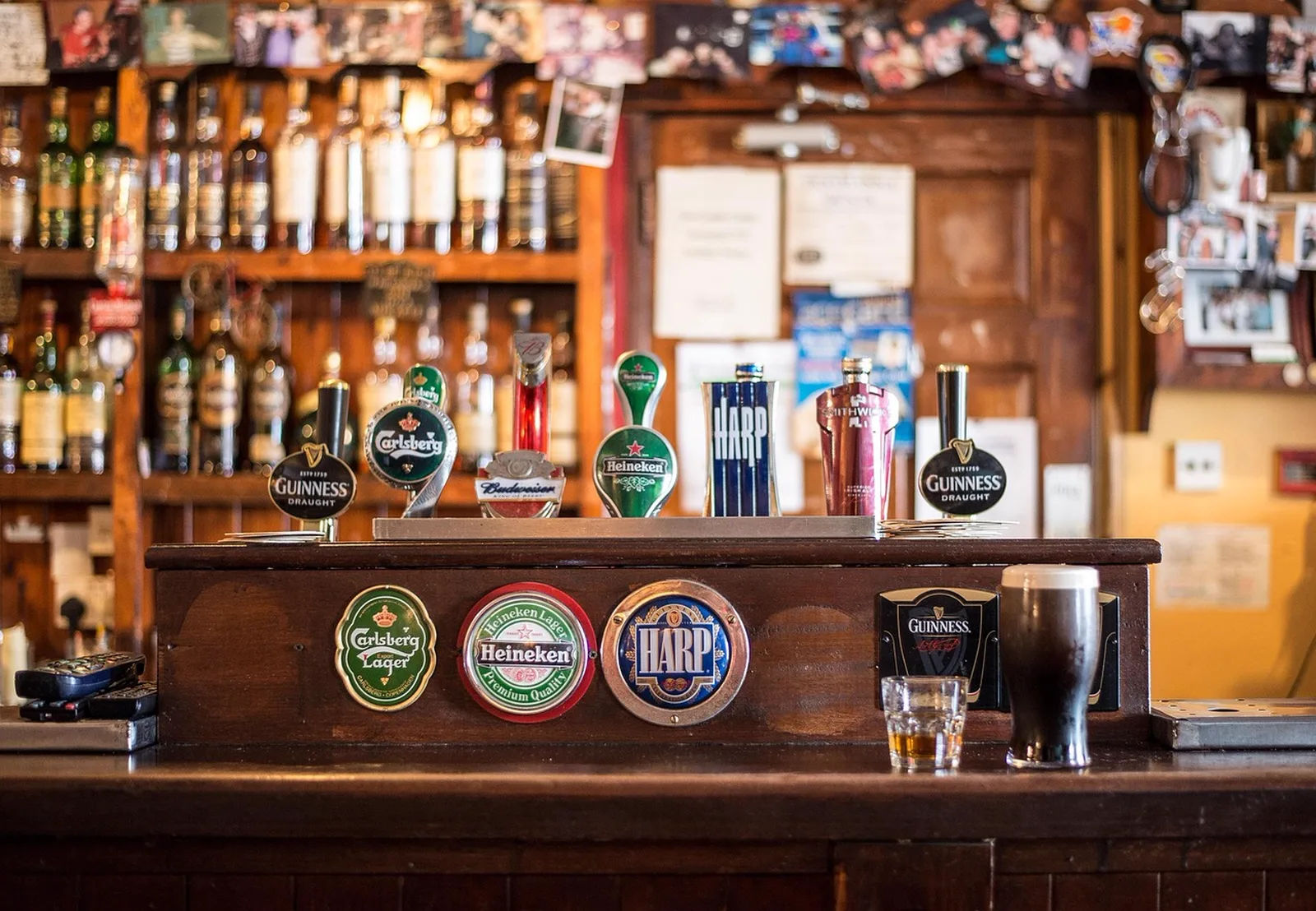 Planet Play Lounge: A wooden pub bar counter featuring draft beer taps, a pint of stout, and liquor bottles on shelves in the background.