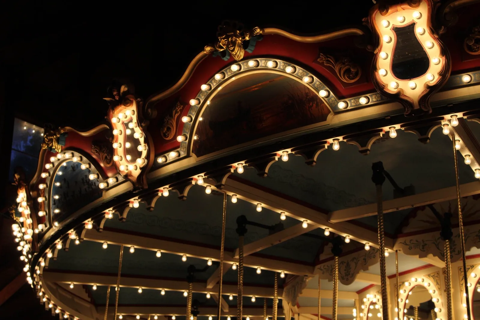 Queen Watevra's Carousel: The ornate canopy and light bulbs of an illuminated vintage carousel at night.