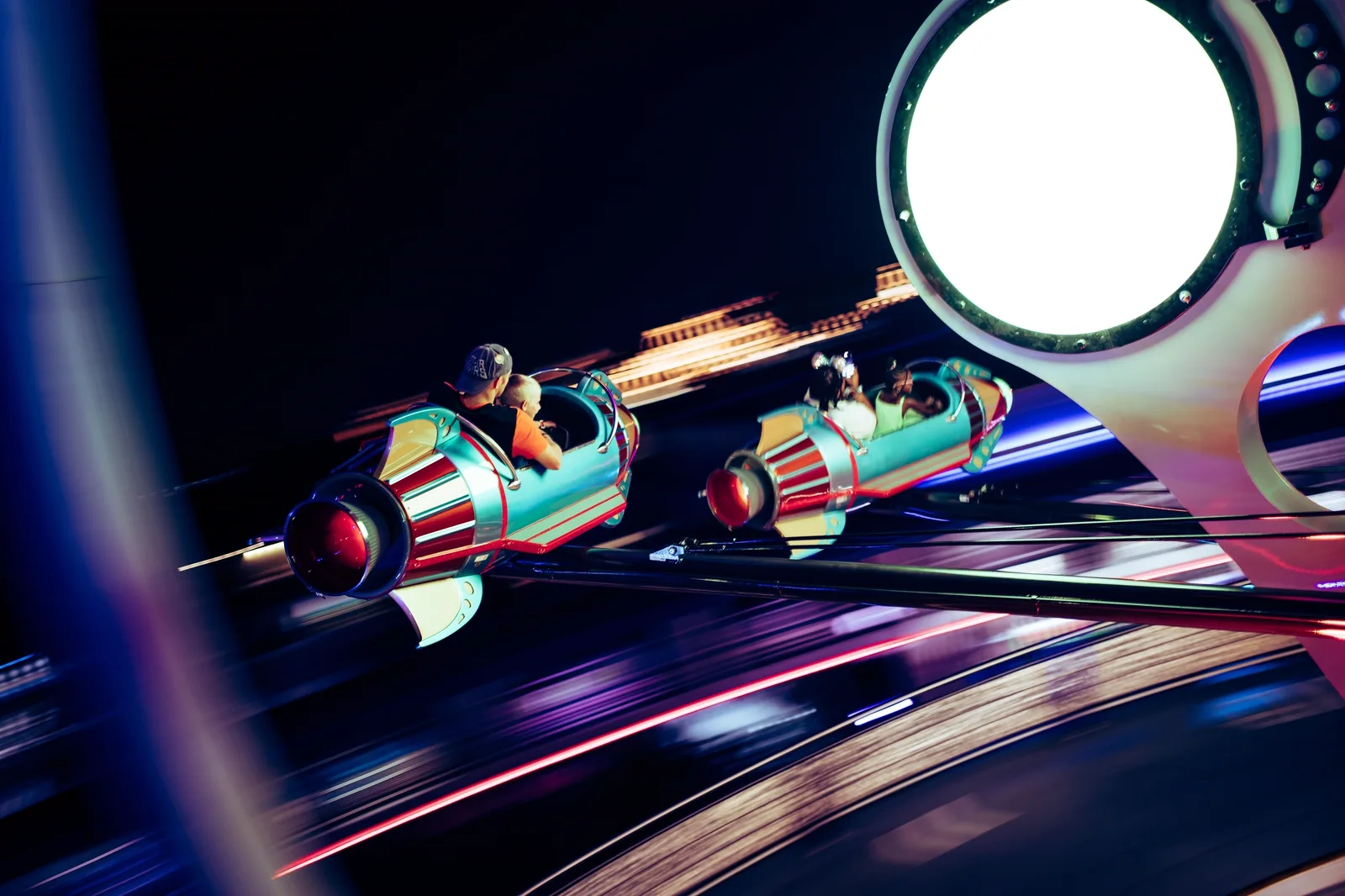 Skull Island: Reign of Kong: People riding in colorful rocket-shaped vehicles on a fast-moving amusement park ride at night.