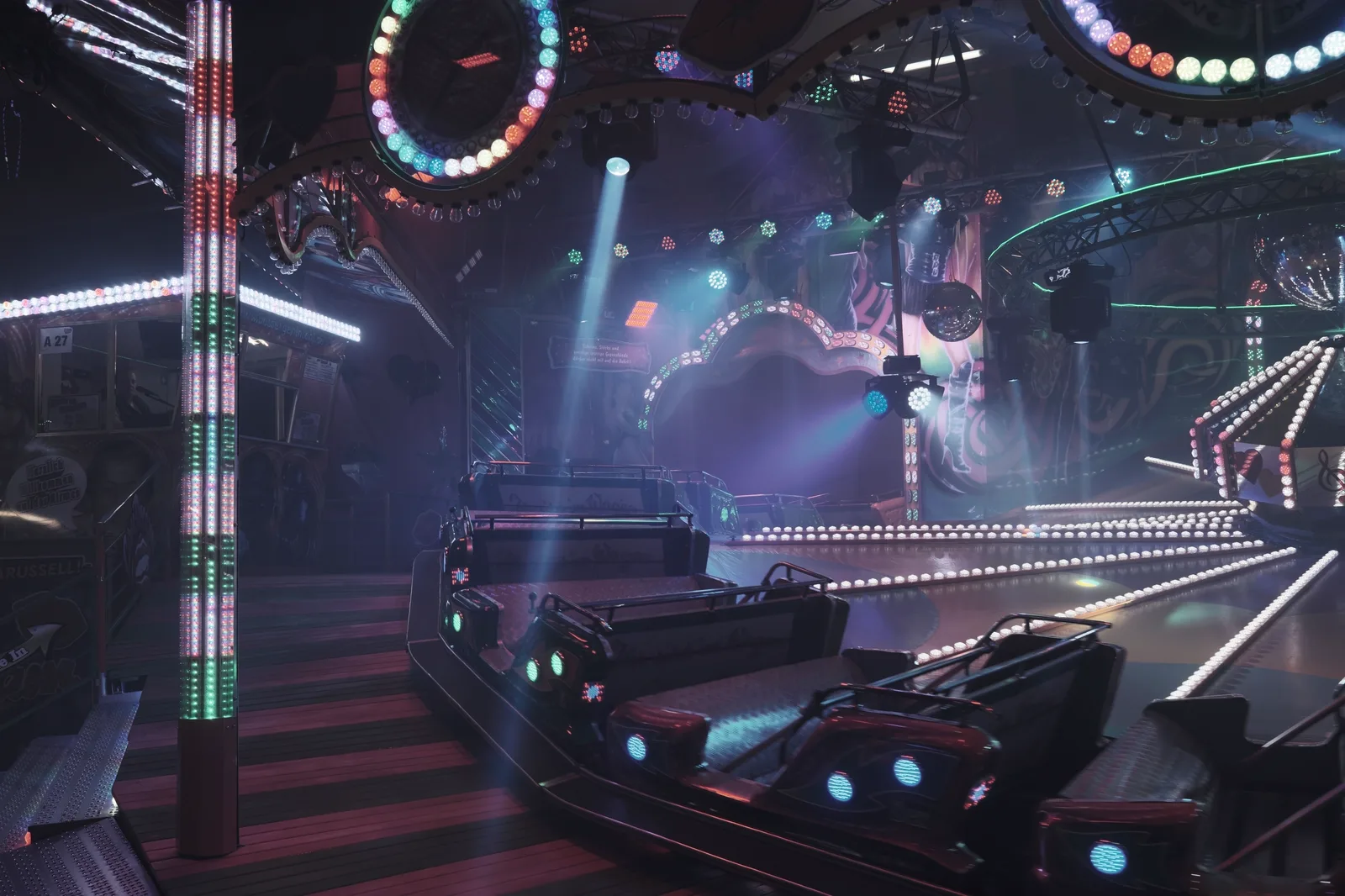 Monsters Unchained: The Frankenstein Experiment: An empty indoor amusement park ride illuminated with colorful neon lights and spotlights in a dark hall.
