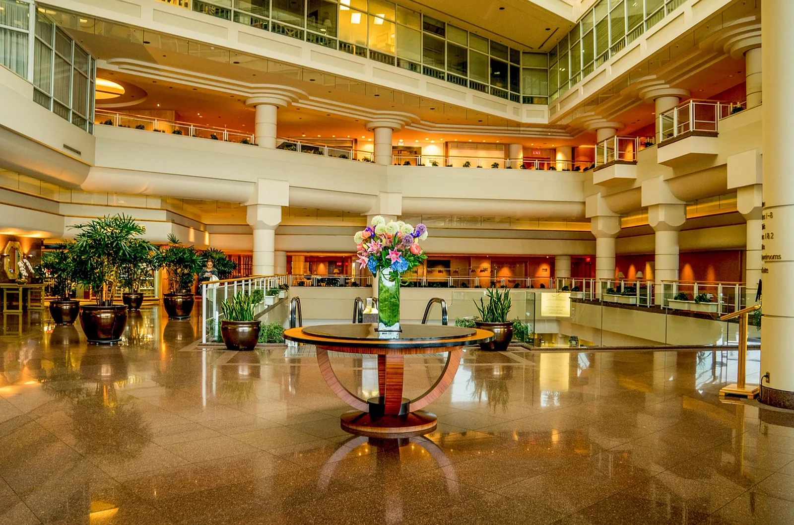 Disney's Riviera Resort: A grand hotel lobby atrium with polished granite floors, multi-level balconies, and a central table with a large flower arrangement.