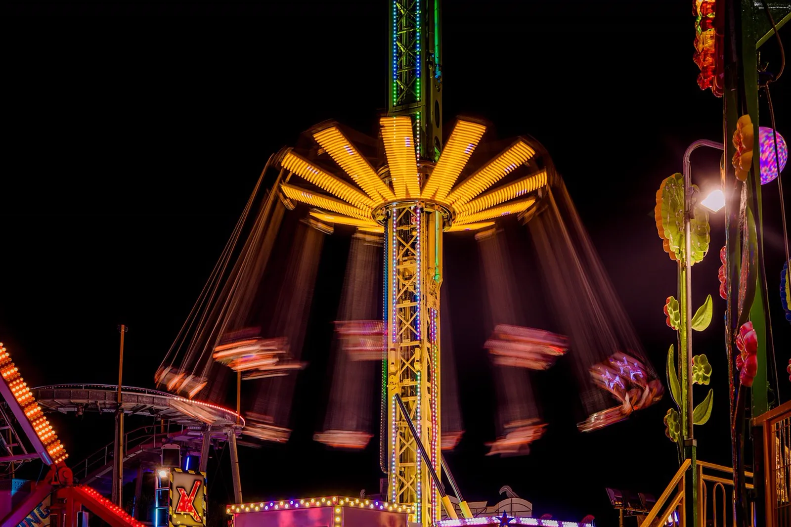 The Twilight Zone Tower of Terror: A illuminated swing tower ride spins at night at an amusement park with motion-blurred seats.