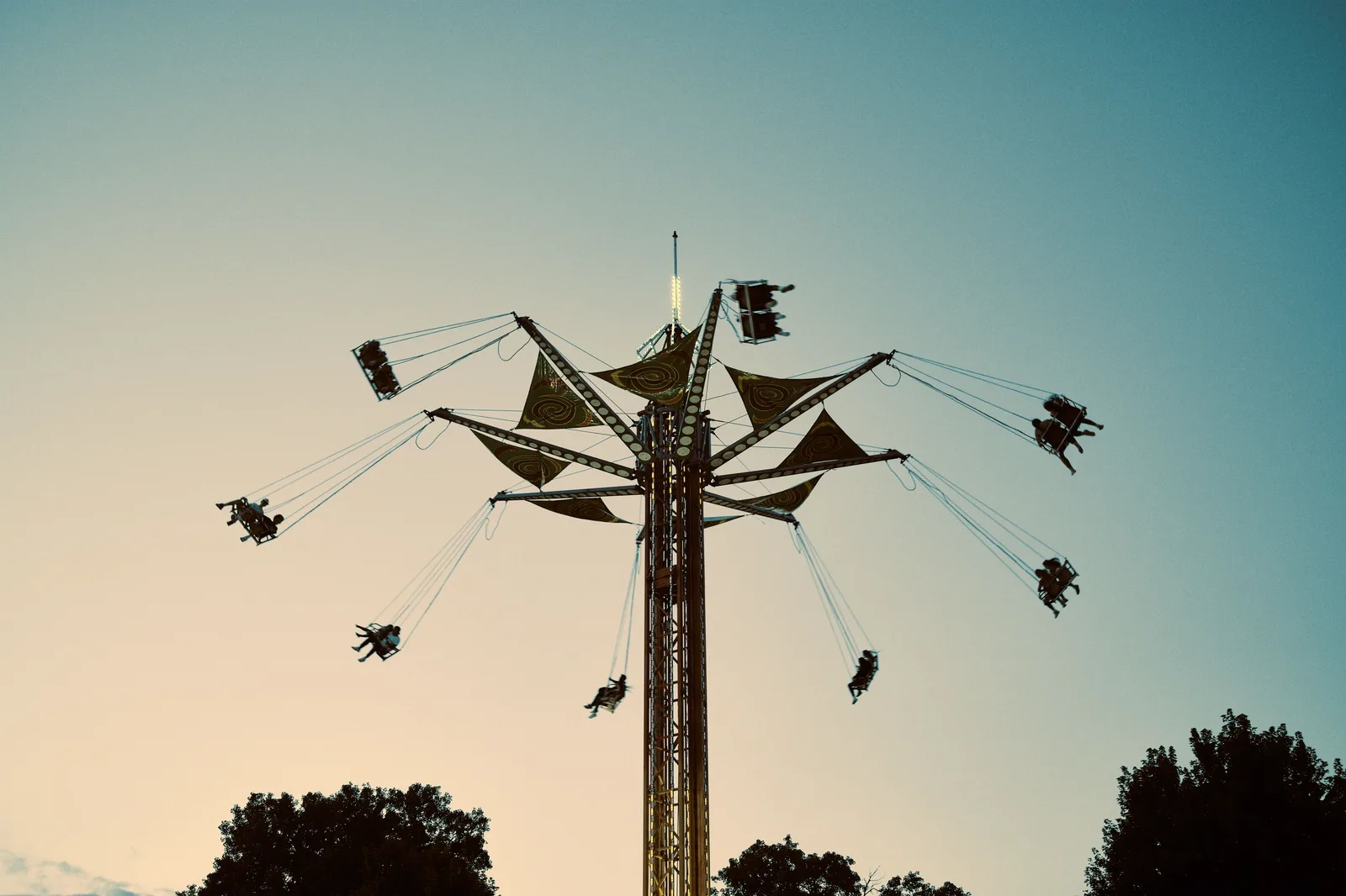 Falcon's Fury: A tall swing tower ride spins riders high in the air against a gradient sky at dusk.