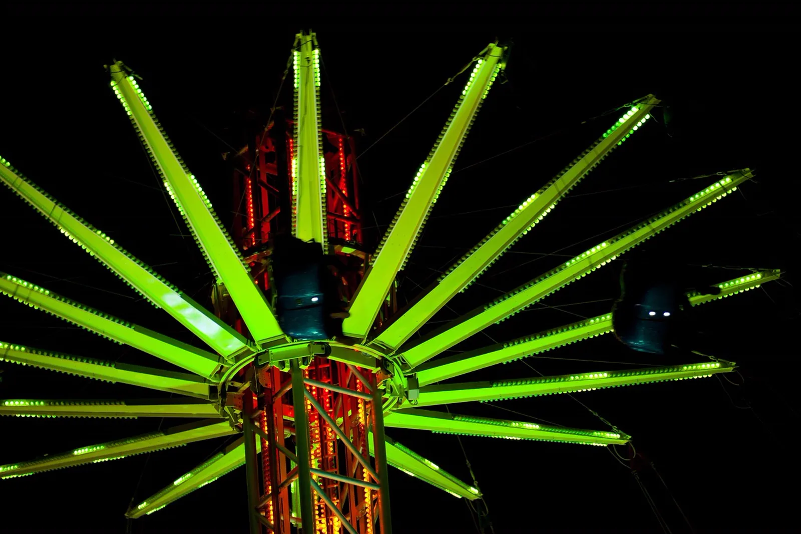 Ko'okiri Body Plunge: Bright green and red lights illuminate a tall amusement park swing tower ride against the dark night sky.