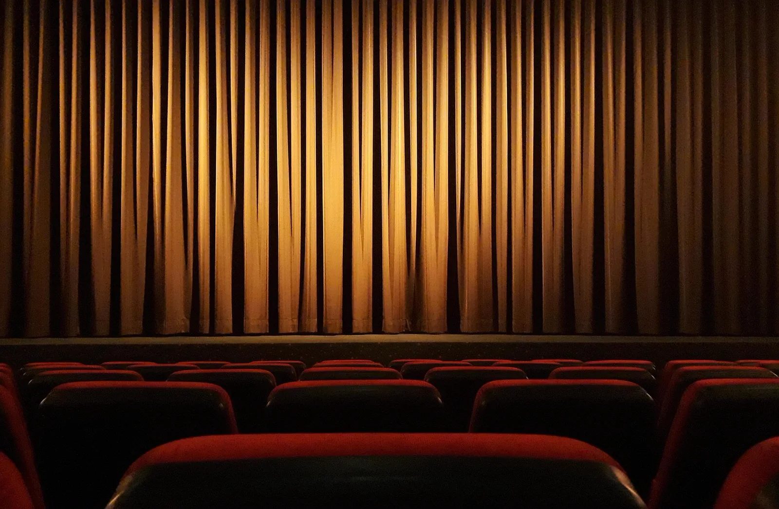 The Bourne Stuntacular: Empty red seats face a lit golden curtain covering a movie theater screen.