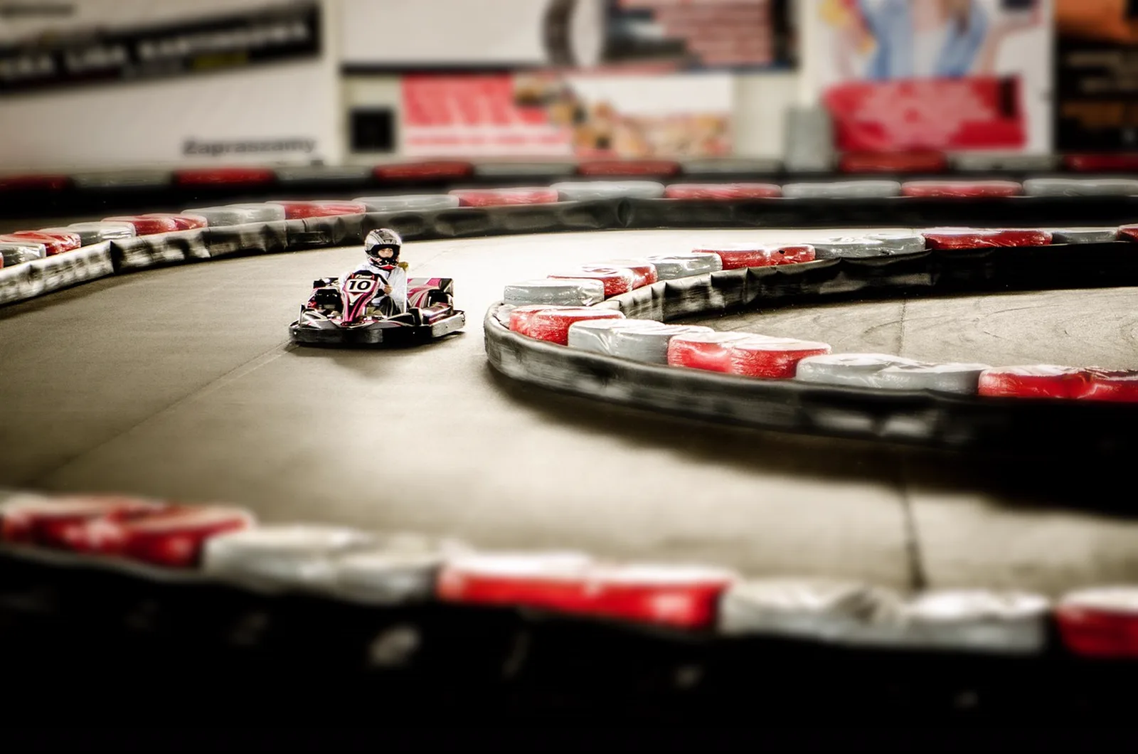 Imagination Zone: A young driver navigates a go-kart around a curved indoor track lined with safety barriers.