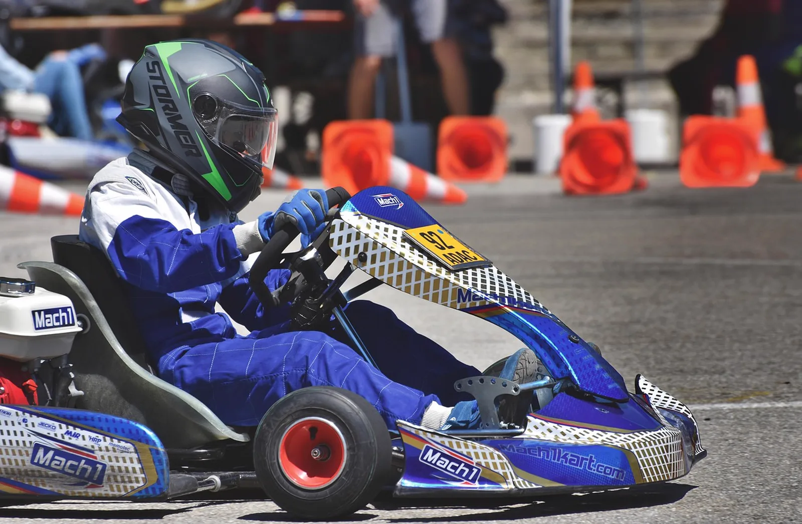 Riptide Racers: A person in a helmet and blue racing suit drives a blue and white go-kart on an outdoor asphalt track.