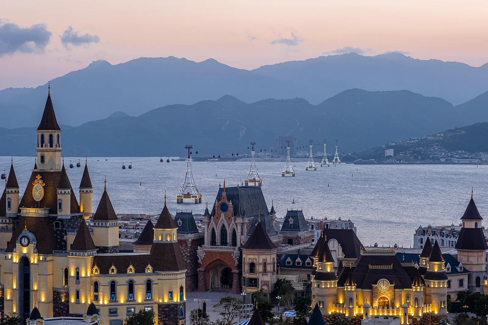 Factory: Castle-style theme park buildings along a waterfront at dusk with mountains in the background.