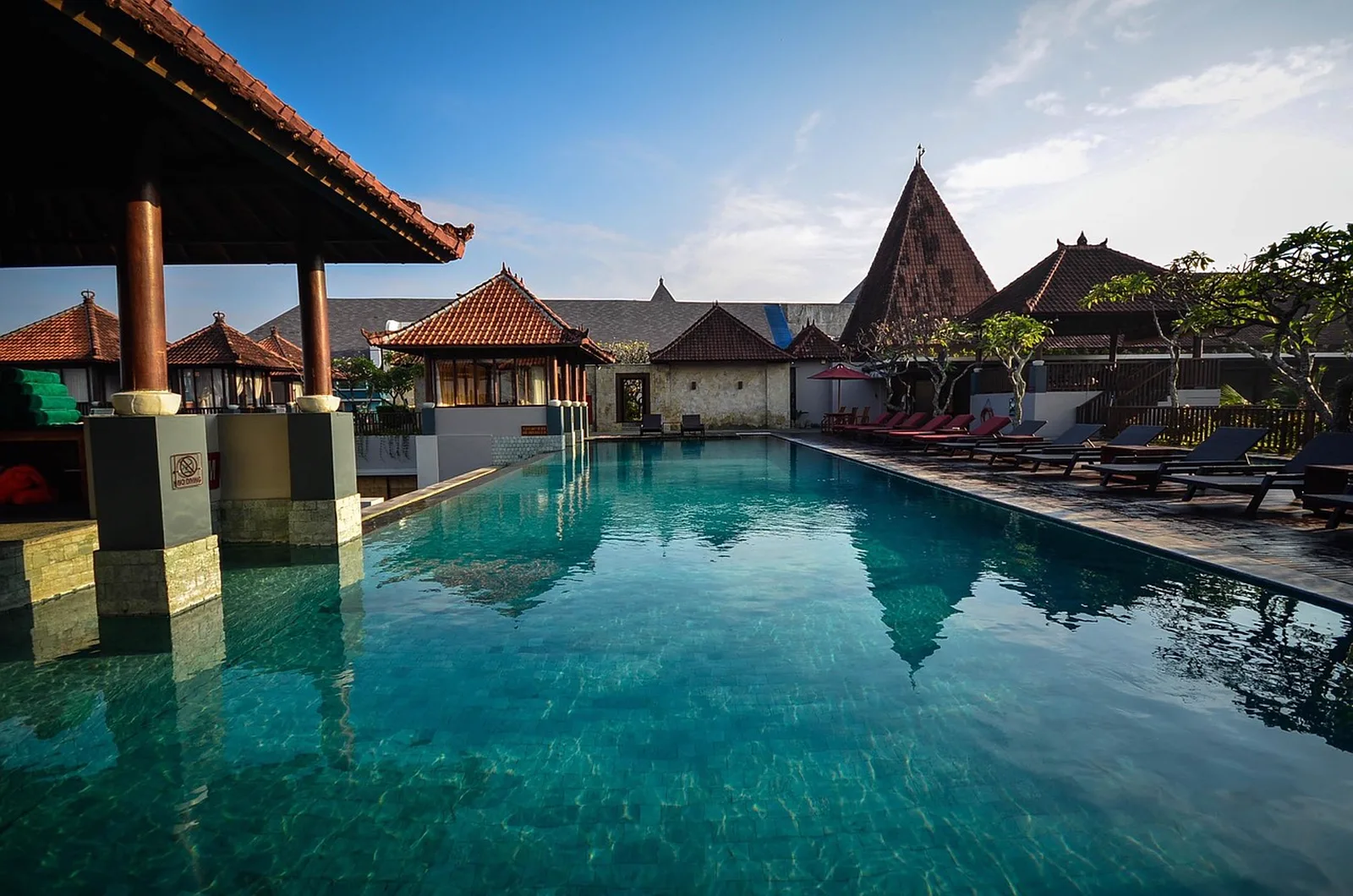 Disney's Coronado Springs Resort: A long outdoor resort swimming pool surrounded by traditional thatched pavilions and sun loungers under a blue sky.