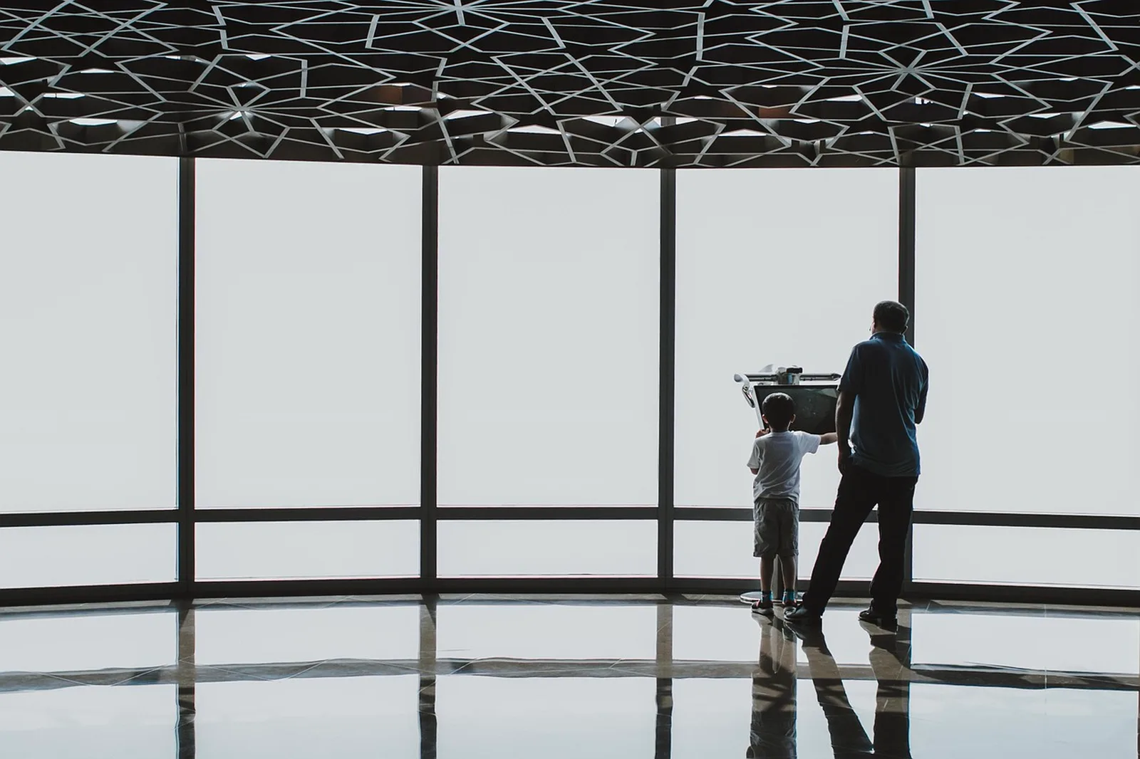 Castle Hill: An adult and child stand in silhouette looking out large floor-to-ceiling windows from an indoor observation deck.
