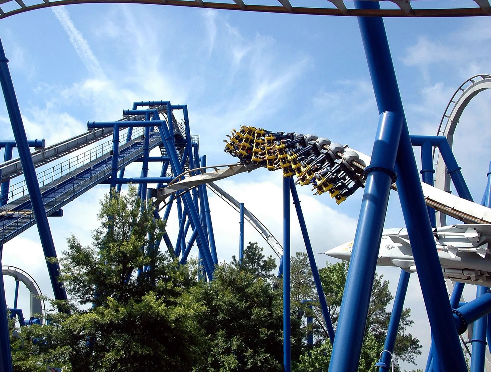 Universal Volcano Bay: A blue roller coaster train travels along a twisted steel track against a partly cloudy sky.