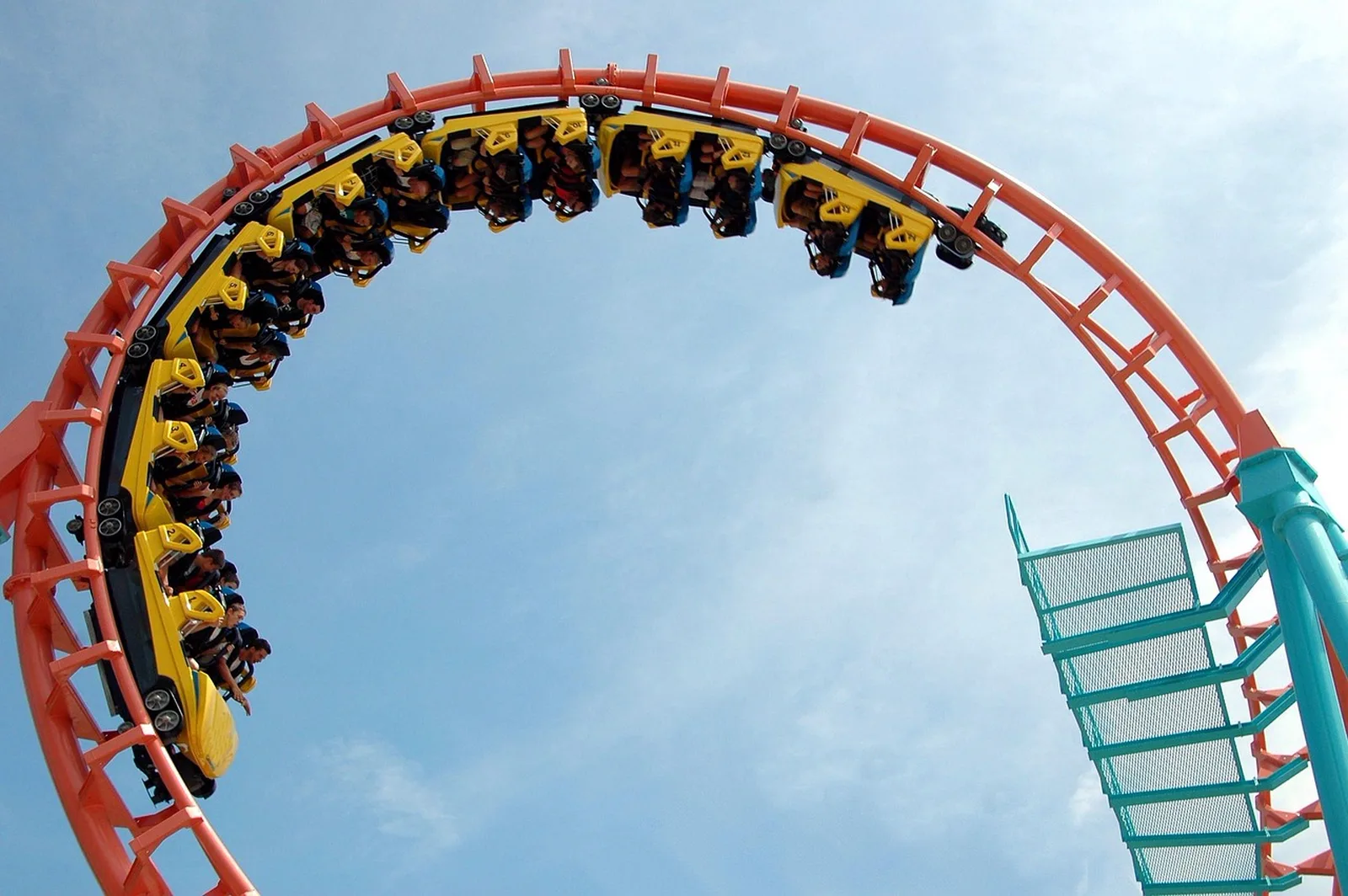 Fast & Furious: Hollywood Drift: A yellow roller coaster train carrying riders travels upside down along an orange track loop against a blue sky.