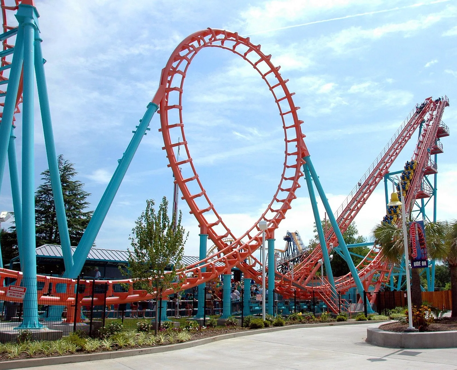 Guardians of the Galaxy: Cosmic Rewind: A bright orange steel roller coaster track with a large loop and blue support towers against a sunny sky.