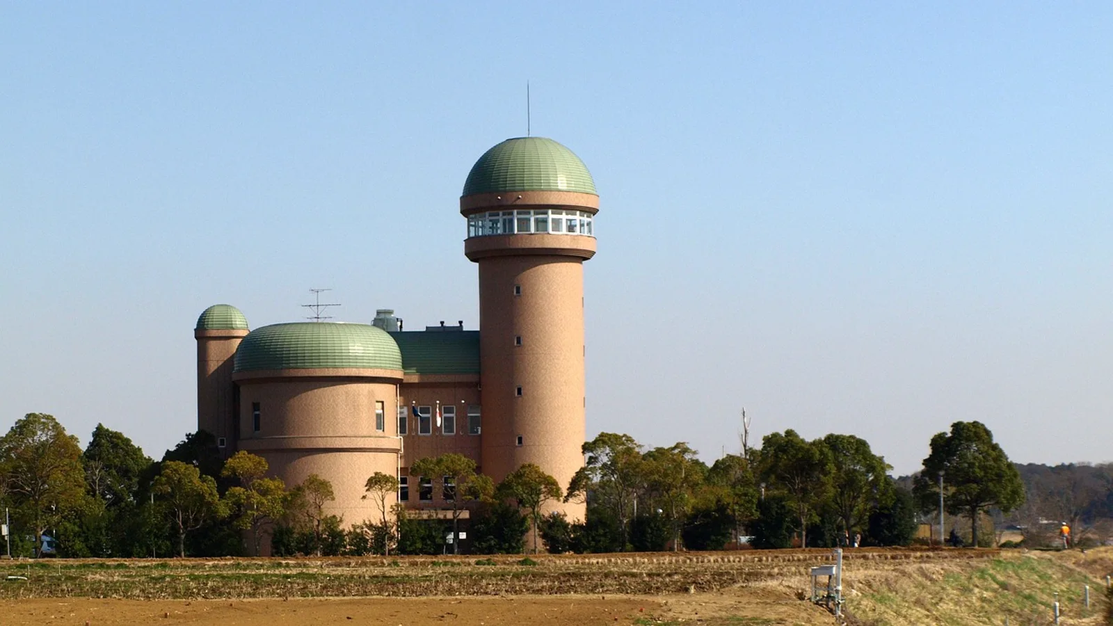 Kennedy Space Center Bus Tour: A tan building with green domed roofs and an observation tower stands under a clear blue sky.
