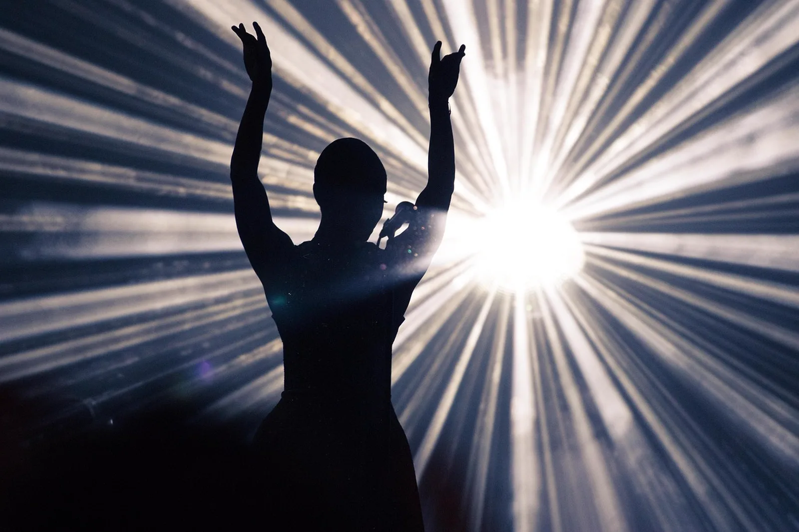 The Untrainable Dragon: A silhouetted performer stands on stage with hands raised in front of bright stage lights.