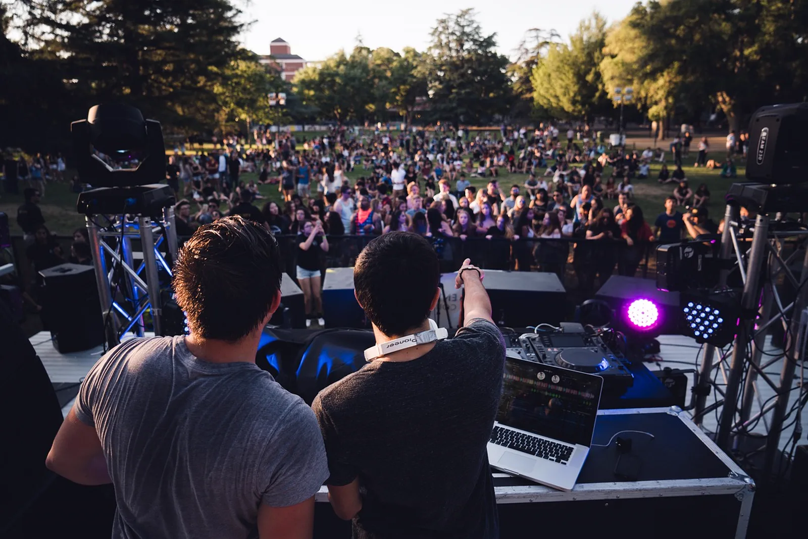 Enchanted Tales with Belle: Two DJs perform on an outdoor stage facing a large crowd gathered on a park lawn.