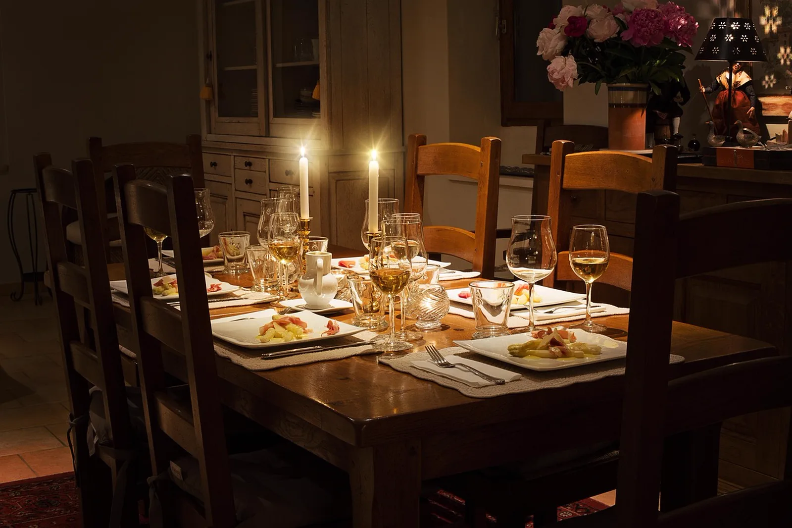Le Cellier Steakhouse: A rustic wooden dining table set with white plates, wine glasses, and lit candles in a warm, dimly lit room.