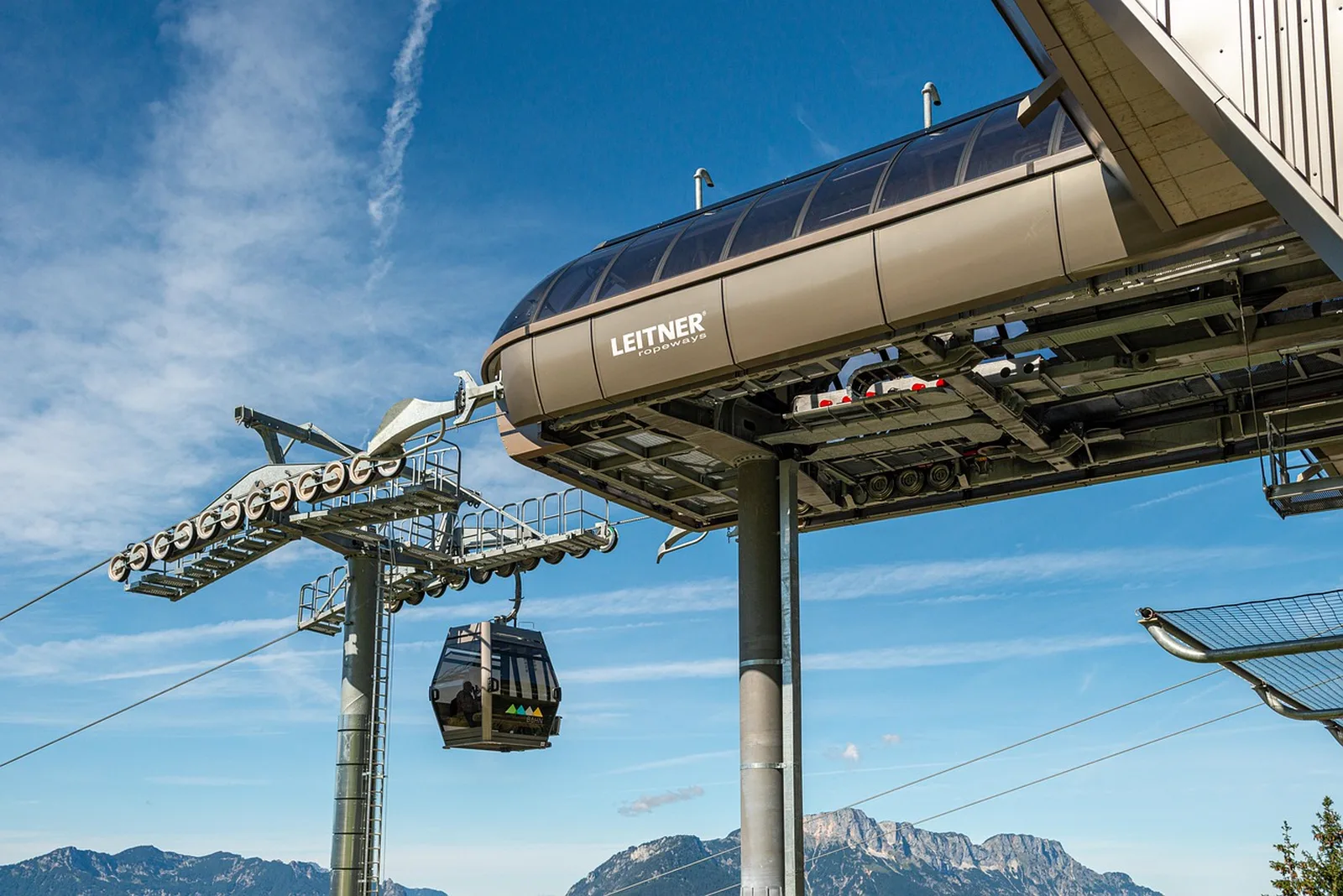 SkyRide: A cable car gondola cabin approaches a Leitner ropeways station terminal against a blue sky.