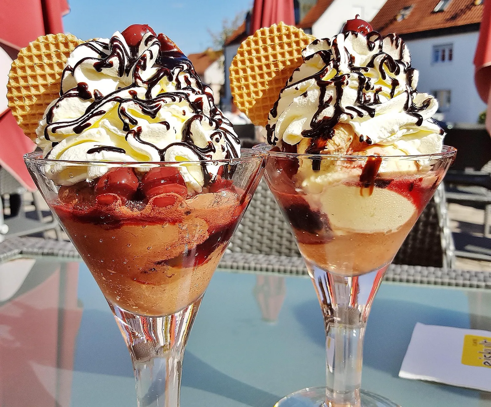 Gator Gully General Store: Two ice cream sundaes topped with whipped cream, chocolate syrup, cherries, and waffle cookies sit on a glass outdoor table.