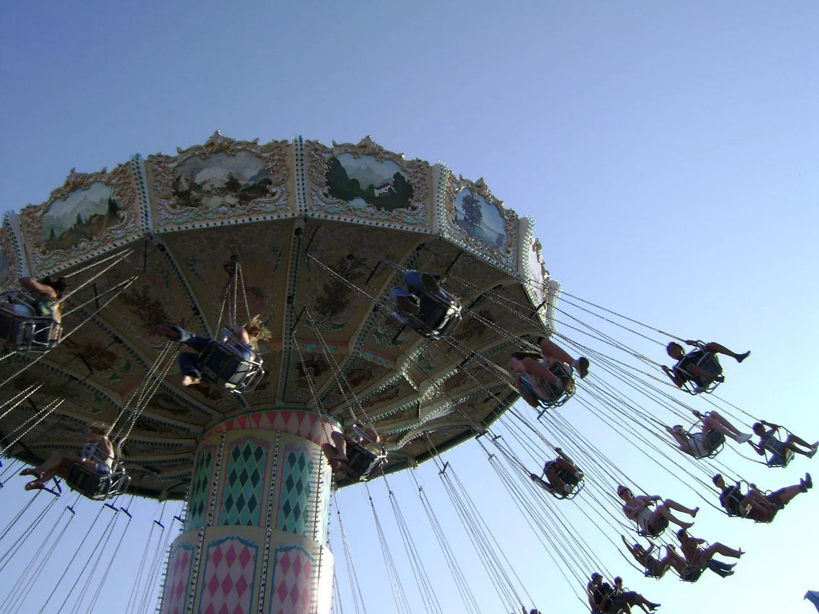 Silly Symphony Swings: A low-angle view of a colorful chair swing ride spinning riders high in the air against a clear blue sky.