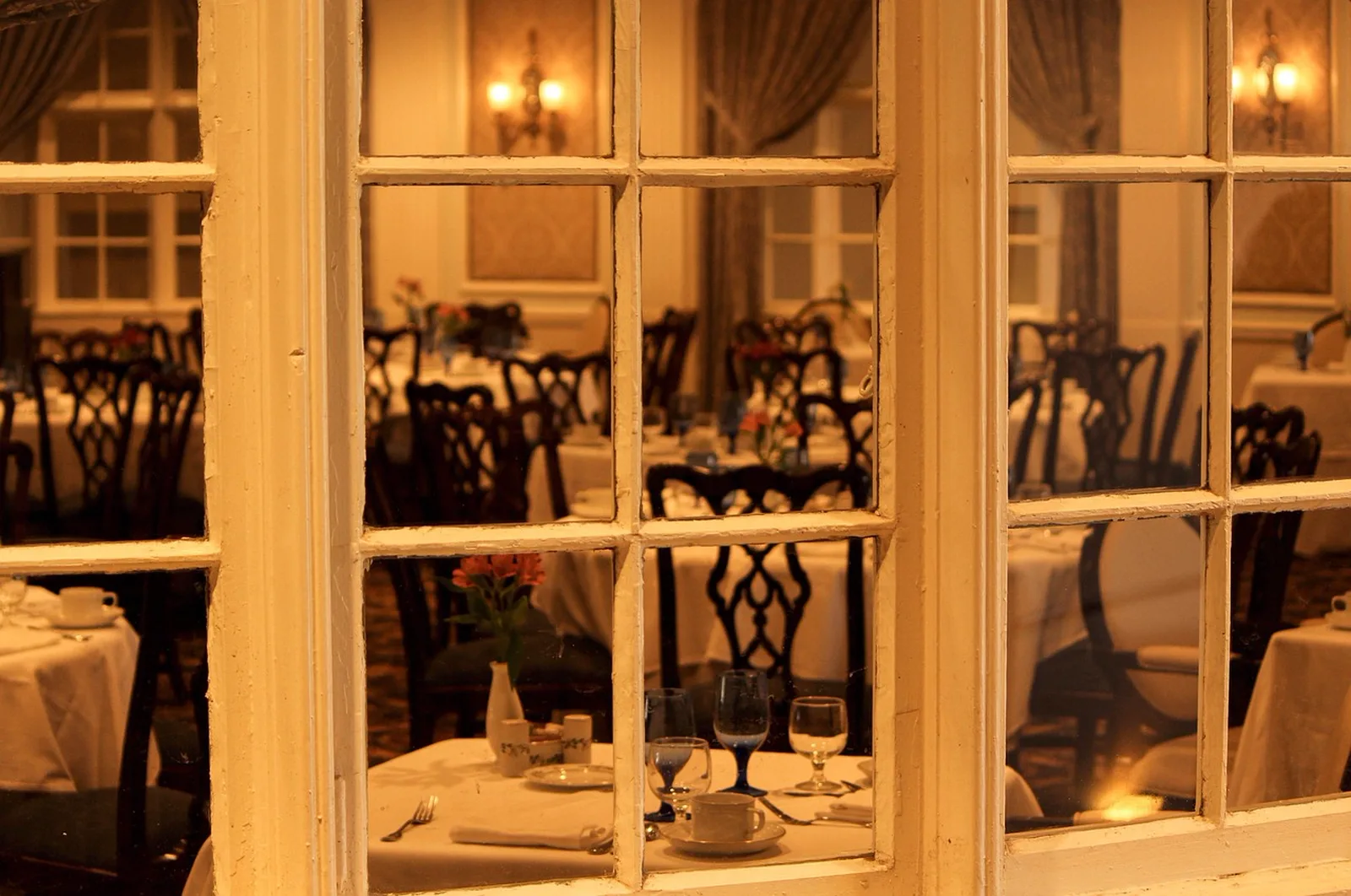'Ohana: A view through multi-pane windows of set dining tables inside an elegant restaurant.