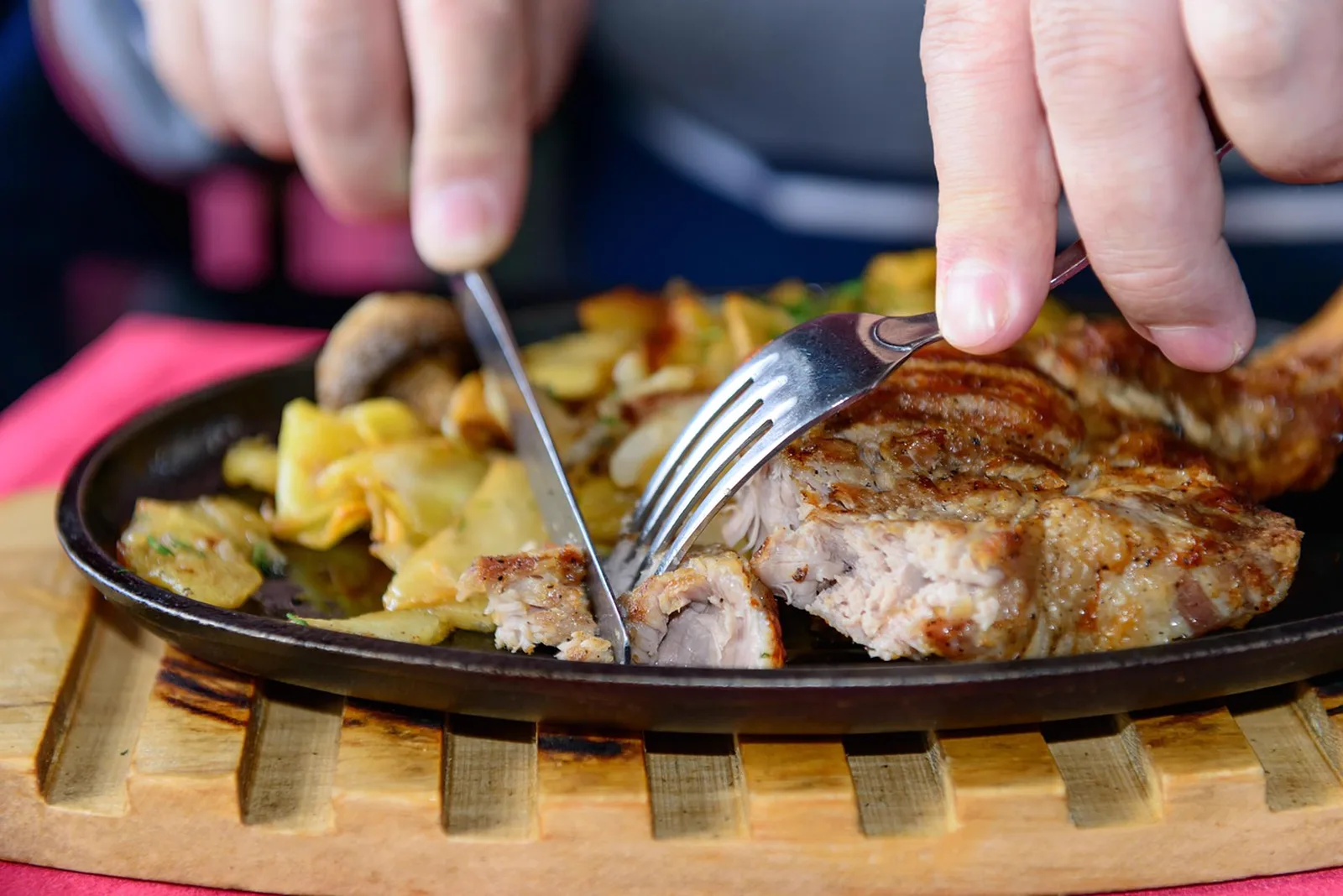 Bricks Family Restaurant: A close-up shot of hands using a fork and knife to cut into a steak served on a skillet with potatoes.