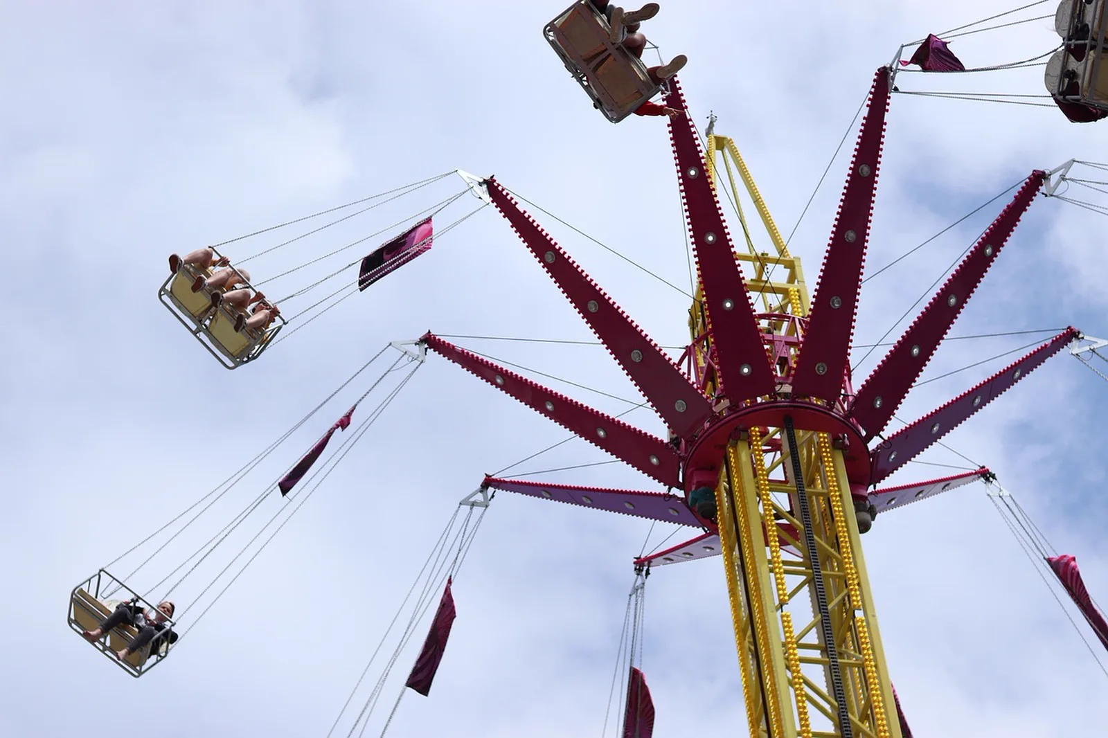 Pantopia: A tall swing tower amusement ride spins riders high in the air against a cloudy sky.