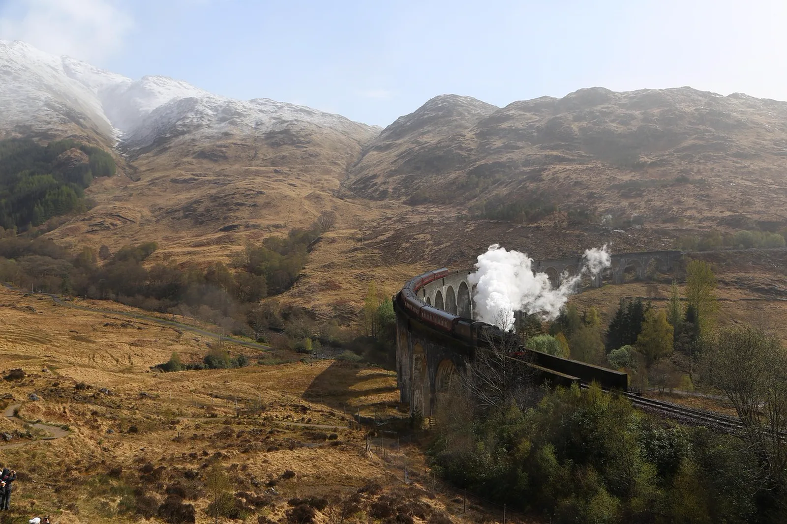 Gatorland Express and Park Grounds: A steam train emitting a plume of white smoke crosses a curved stone viaduct surrounded by mountains.