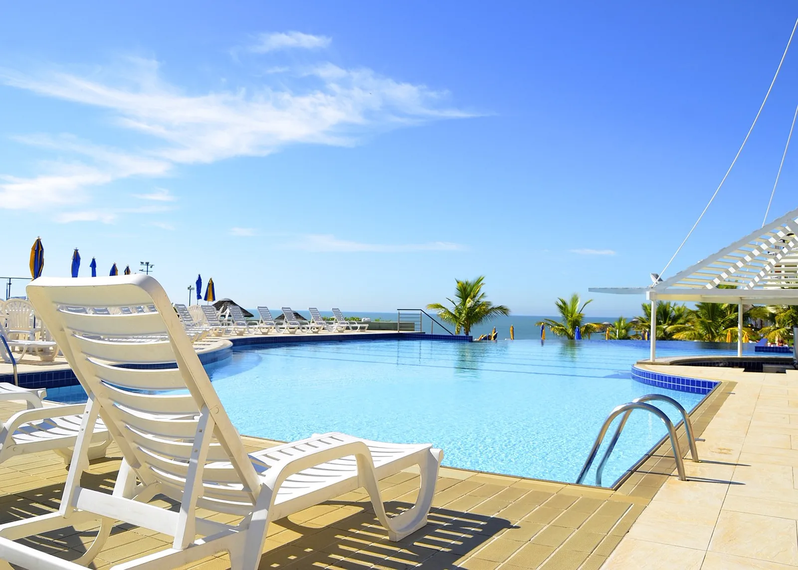 Universal Endless Summer Resort, Surfside Inn and Suites: A white plastic lounge chair sits beside an outdoor swimming pool overlooking the ocean under a clear blue sky.